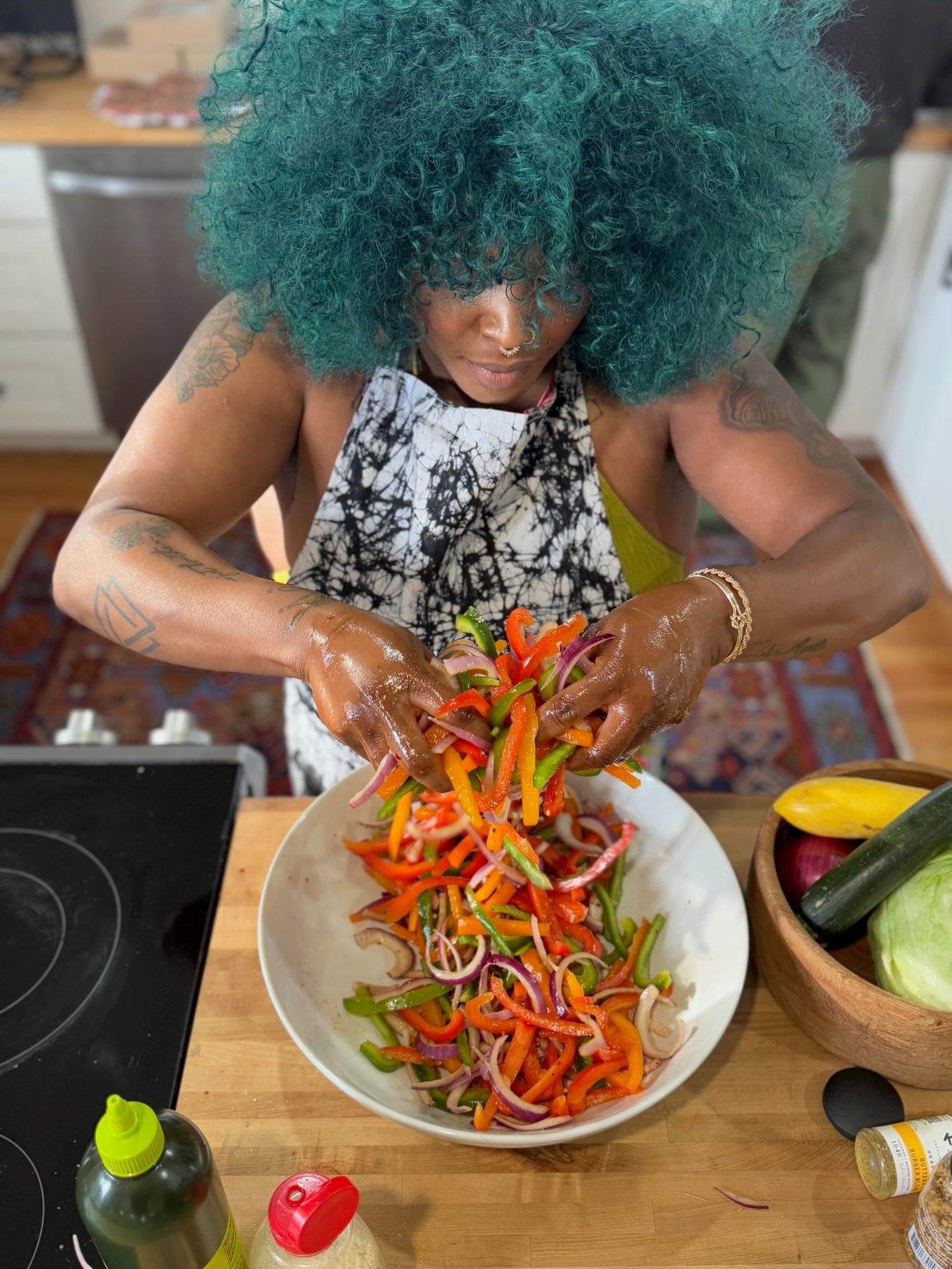A woman wearing the Echo apron mixes a vibrant bowl of red, yellow, and green bell peppers, ready for the grill or stir-fry—capturing motion and color in the kitchen.